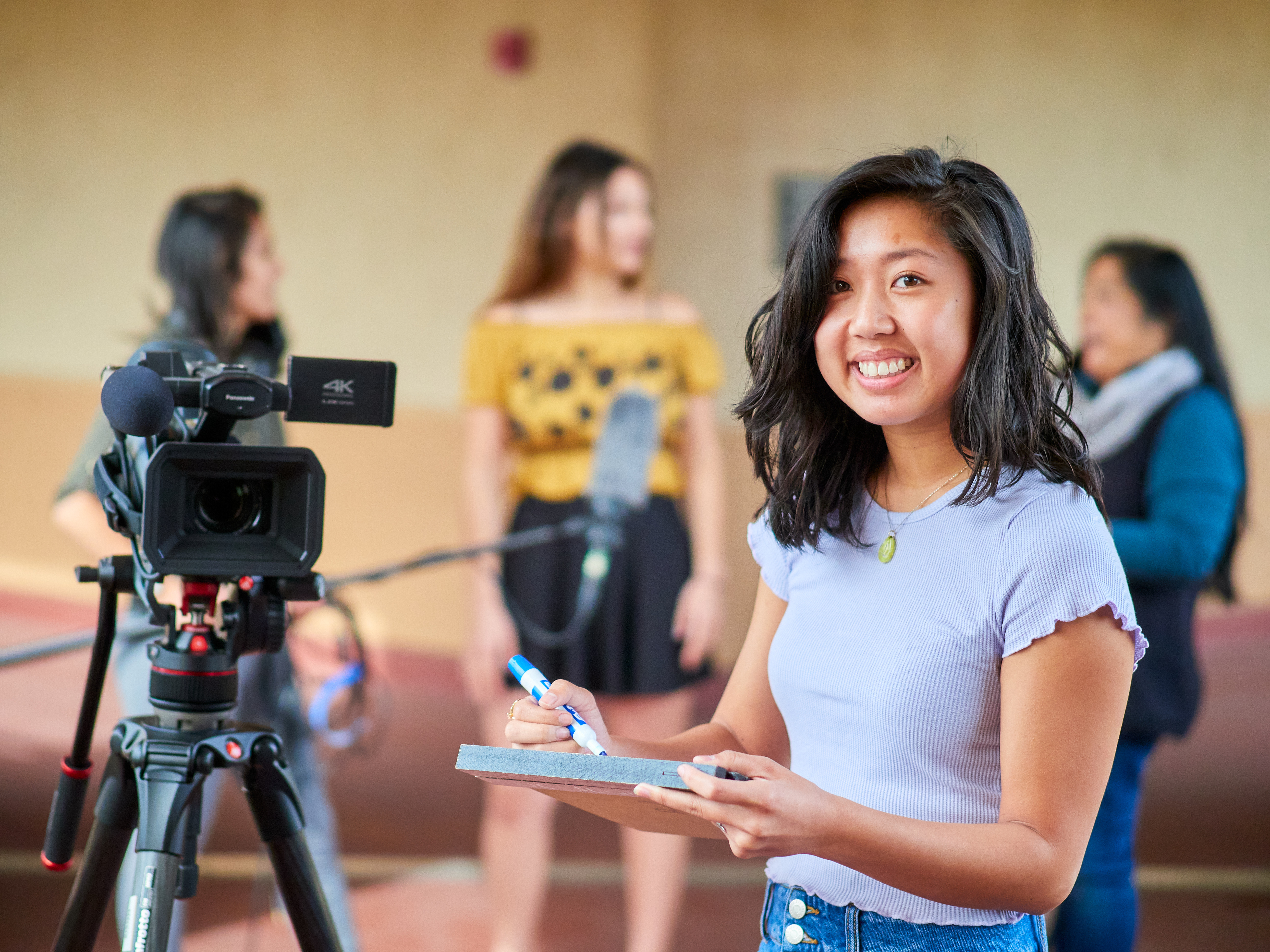 A student smiling and making notes next to a video camera