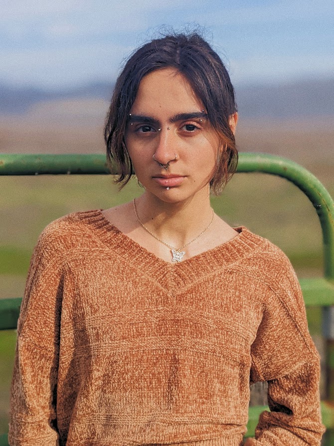 Photo of two-spirit Cash Martinez of Pomo Band, in an open field wearing a brown knit sweater 